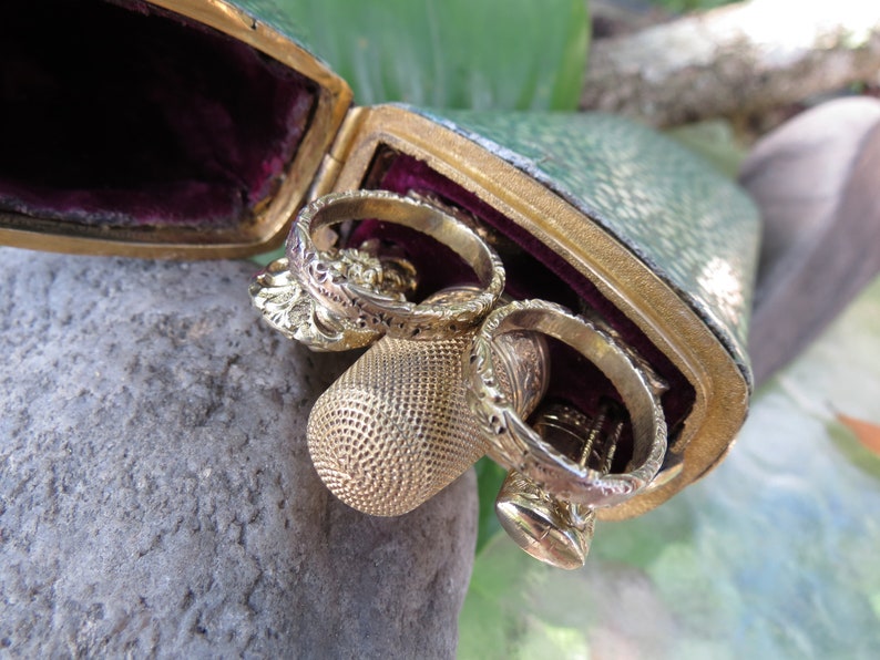 May include: A green leather case with gold trim and a velvet lining, containing three gold thimbles and a gold ring.