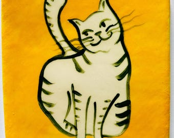 May include: A square ceramic tile with a vibrant yellow background featuring a hand-painted illustration of a white cat with dark green stripes. The cat is depicted in a seated position with its tail raised, showcasing simple brushstroke details.