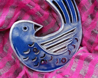 May include: A ceramic bird ornament featuring a glossy blue glaze with dark blue and black hand-painted details. The bird is depicted in a curved, stylized posture with visible wing and feather markings, showcasing a smooth, reflective finish.