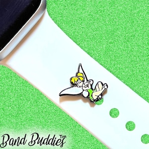 May include: A colorful enamel charm featuring Tinkerbell, in green and yellow, attached to a white watch band. The charm is a Disney-themed accessory. The words "Band Buddies" are in the lower left corner.