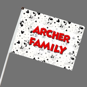 May include: A white flag with a repeating pattern of Mickey Mouse illustrations and black stars. The words "ARCHER FAMILY" are in large, red, 3D letters across the center. The flag is attached to a white pole with a gold tip.
