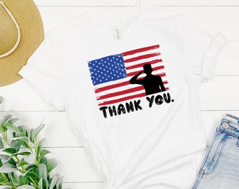 May include: White t-shirt with a red, white, and blue American flag design and a silhouette of a soldier saluting. The text "THANK YOU." is below the flag.
