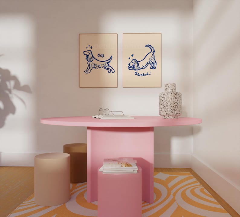 May include: A pink oval table with a matching pink base, two beige cylindrical stools, and a small pink square table. Two framed dog illustrations hang on the wall. A speckled vase sits on the table. The rug has an orange and white pattern.