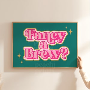 Może przedstawiać: Oprawiony wydruk artystyczny z napisem "Fancy a Brew?" w różowych i białych literach na turkusowym tle. Złote rozbłyski gwiazd podkreślają design. Wydruk jest w drewnianej ramie.