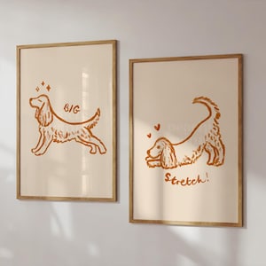 May include: Two framed art prints featuring line drawings of a dog in a playful pose. One print has the word "BIG" and sparkles, the other says "Stretch!" with hearts. The artwork is in shades of brown on a cream background.