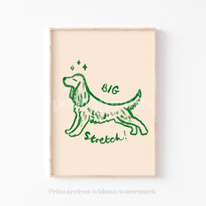 May include: A framed print featuring a green line drawing of a dog in a stretching pose. The words "BIG Stretch!" are written above and below the dog. The background is a light beige color.