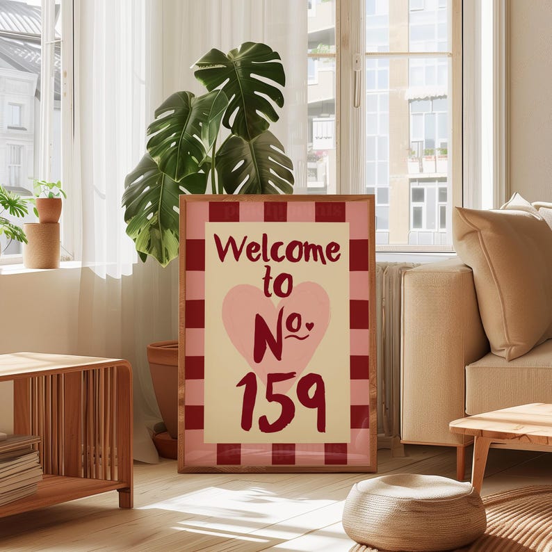 May include: A framed sign with the text "Welcome to No. 159". The design includes a pink heart and a red and pink checked border. The sign is in a wooden frame, creating a welcoming feel.