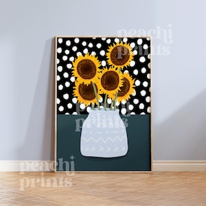 May include: A framed print of a bouquet of yellow sunflowers with brown centers in a light blue vase with a white geometric pattern. The background is a black and white polka dot pattern.