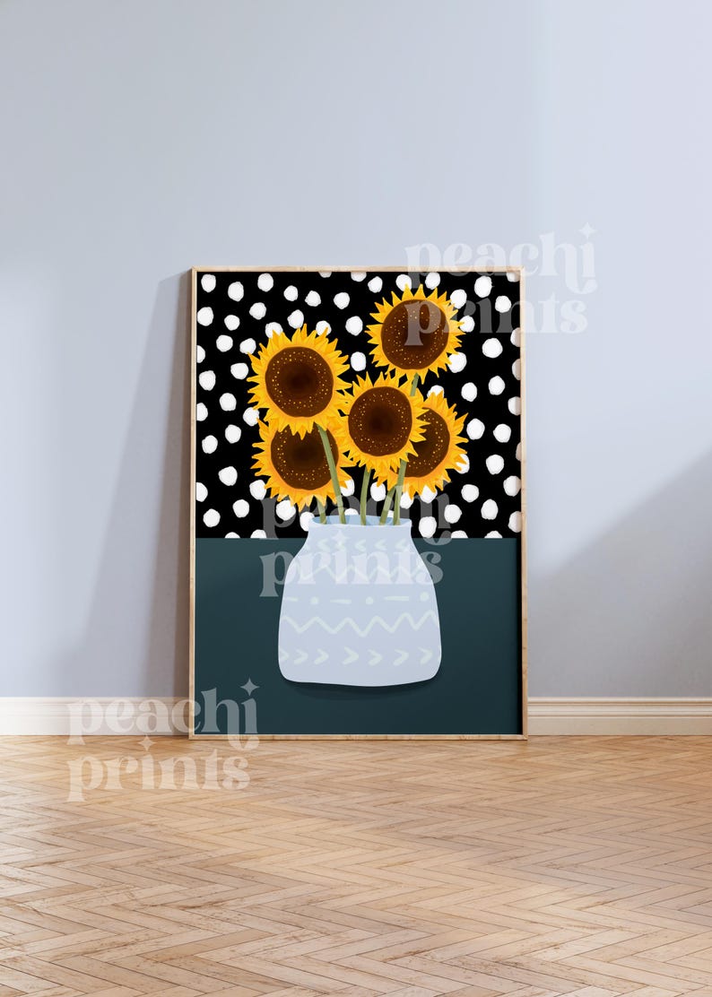 May include: A framed print of a bouquet of yellow sunflowers with brown centers in a light blue vase with a white geometric pattern. The background is a black and white polka dot pattern.