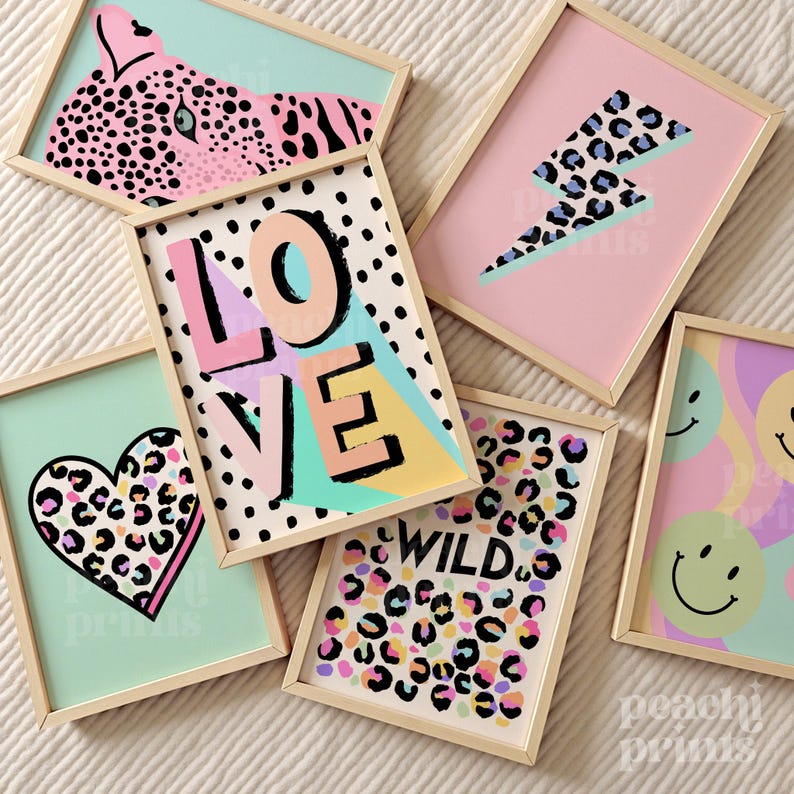 May include: A collection of framed art prints with a playful, modern aesthetic. Designs include a pink leopard, a lightning bolt, a heart, the word "LOVE", the word "WILD", and smiley faces. Each print has a wooden frame and a colorful background.
