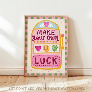 Könnte beinhalten: Gerahmter Kunstdruck mit einem rosa Spielautomaten-Design und den Worten "MAKE your own LUCK". Das Kunstwerk enthält ein Herz, ein Smiley und ein vierblättriges Kleeblatt. Der Rahmen hat einen rosa und grünen Karomuster-Rand.