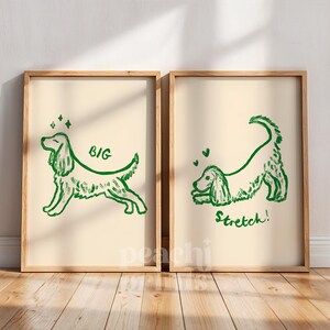 May include: Two framed art prints with a light beige background. Each print features a green line drawing of a dog. One print says "BIG" and the other says "Stretch!". The frames are made of light brown wood.