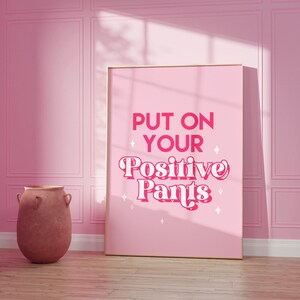 May include: A pink poster with the text "PUT ON YOUR POSITIVE PANTS" in a pink retro font with white stars around the text.
