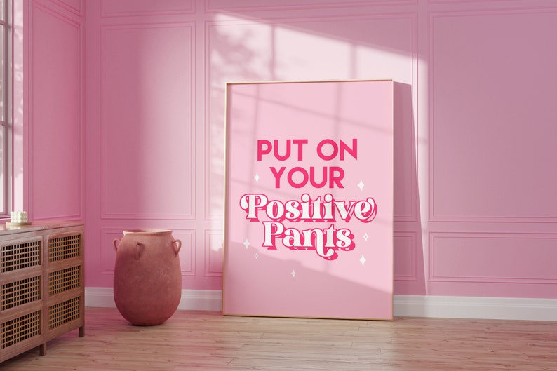 May include: A pink poster with the text "PUT ON YOUR POSITIVE PANTS" in a pink retro font with white stars around the text.