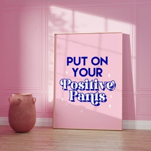 May include: A pink framed poster with the text "PUT ON YOUR Positive Pants" in blue and white lettering with white stars on a pink background.