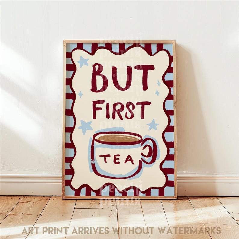 May include: A framed art print with the words "BUT FIRST TEA" in burgundy lettering. The print features a cream-colored background with a tea cup illustration and blue star accents, set against a red and blue border.