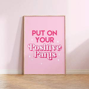 May include: A pink framed poster with the text "PUT ON YOUR Positive Pants" in pink and white lettering with white stars on a pink background.