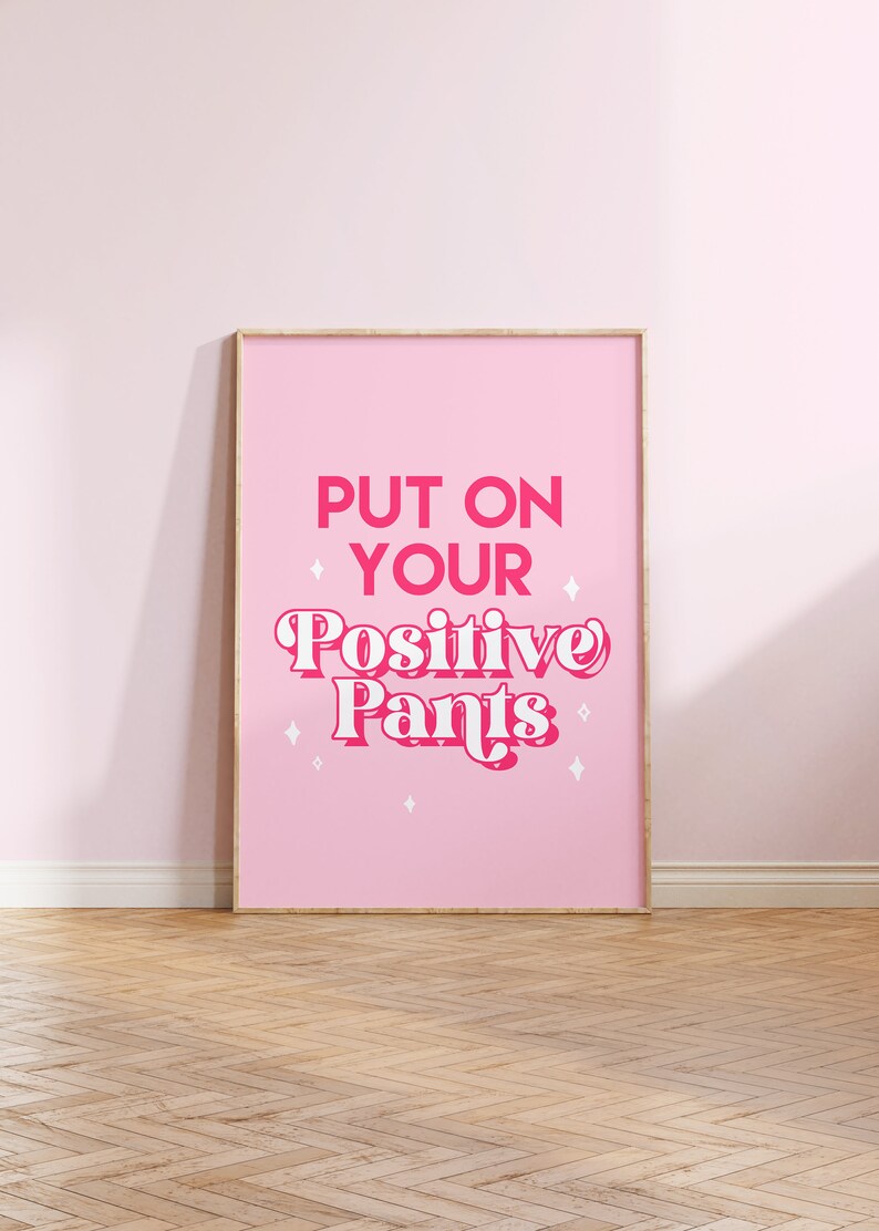 May include: A pink framed poster with the text "PUT ON YOUR Positive Pants" in pink and white lettering with white stars on a pink background.