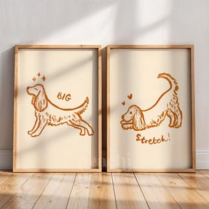 May include: Two framed prints with a light beige background and a brown dog illustration. One print says "BIG" and the other says "Stretch!". The dog illustrations are in a playful, cartoon style, with hearts and stars.