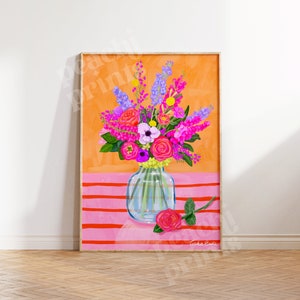 Pode incluir: Um buqu&ecirc; colorido de flores rosa, roxas e brancas em um vaso de vidro transparente sobre um fundo listrado rosa e laranja. O vaso est&aacute; sobre uma superf&iacute;cie rosa com uma &uacute;nica rosa rosa ao lado. O texto "Tasha Evanko" est&aacute; no canto inferior direito da imagem.