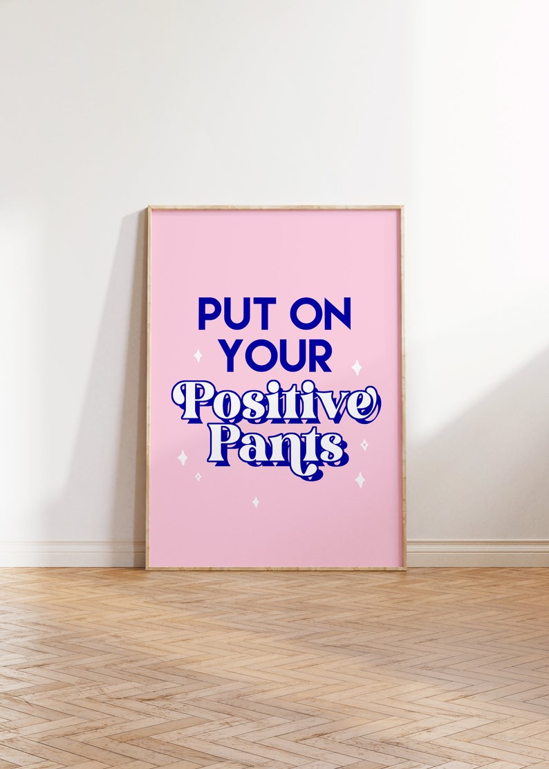 May include: A pink framed poster with the text "Put on your Positive Pants" in blue lettering with white stars.