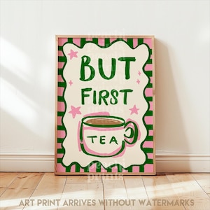 May include: A framed art print with a pink and green border. The print features the words "BUT FIRST TEA" in green, with a teacup illustration. Pink stars and a decorative border surround the text. The phrase "ART PRINT ARRIVES WITHOUT WATERMARKS" is at the bottom.