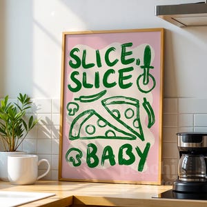 May include: A framed art print with a pink background and green text that reads "SLICE, SLICE, BABY." The print features pizza slices, mushrooms, and chili peppers. A coffee maker and a mug are in the foreground.