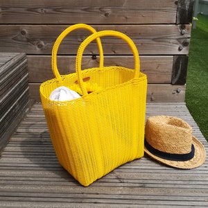リサイクルプラスチックから手編みされた大きな黄色のトートバッグ。丈夫で耐久性があり、買い物バッグやビーチバッグとして最適。ボヘミアンスタイル。
