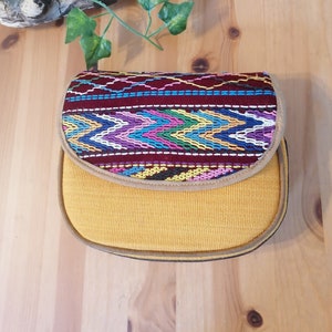 May include: A small, yellow, fabric handbag with a flap closure. The flap is decorated with a colorful, geometric pattern.