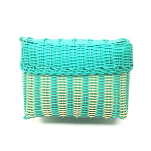 May include: A turquoise woven basket with a light brown woven bottom. The basket is rectangular and has a smooth, polished finish.