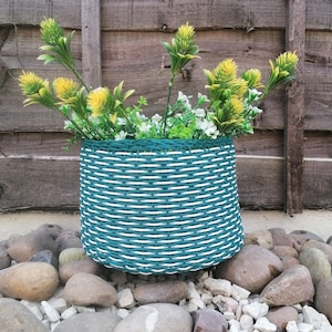 May include: A green and white striped woven planter with a cluster of yellow and white flowers.