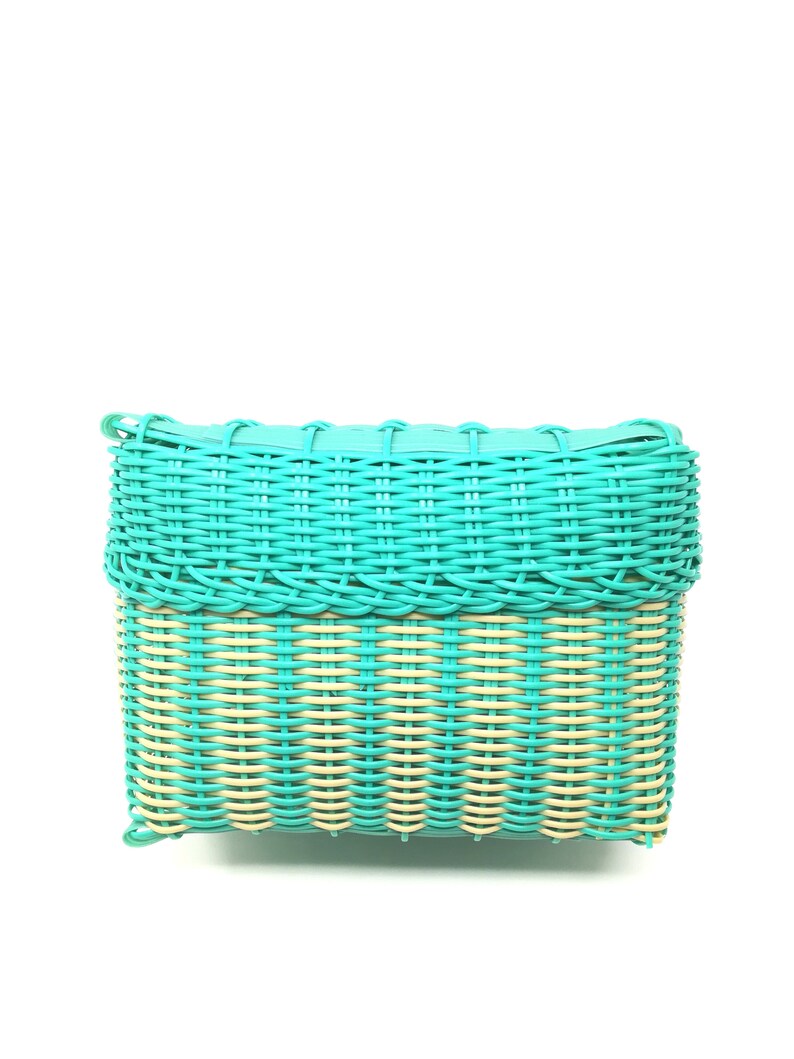 May include: A turquoise woven basket with a light brown woven bottom. The basket is rectangular and has a smooth, polished finish.