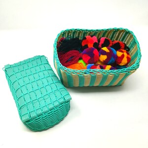 May include: Two turquoise woven baskets, one with a lid, filled with colorful yarn pom-poms. The baskets have a striped pattern.