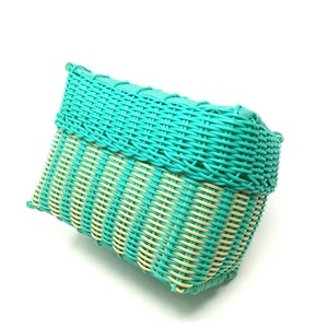 May include: A woven basket with a teal blue and cream striped pattern. The basket is made of plastic and has a rectangular shape.