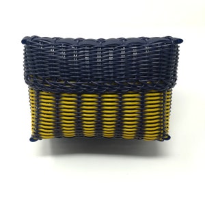 May include: A woven basket with a blue and yellow pattern. The basket is made of a woven material and has a rectangular shape.