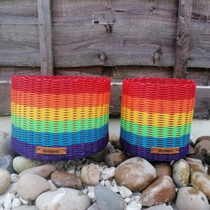 Könnte beinhalten: Zwei regenbogenfarbene geflochtene Körbe mit braunen Lederetiketten, auf denen "VERAPAZ" steht. Die Körbe stehen auf einem Bett aus kleinen weißen Steinen.