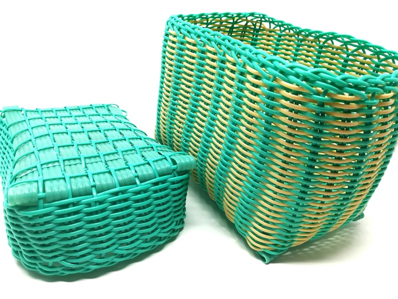 May include: Two woven plastic baskets, one green and one green and yellow. The green basket is smaller and has a square shape. The green and yellow basket is larger and has a rectangular shape.