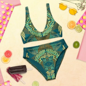 May include: Teal blue bikini with a geometric pattern in yellow and green. The pattern is reminiscent of ancient art.
