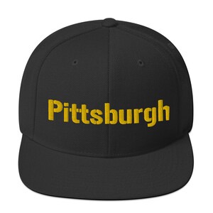 May include: Black baseball cap with the word "Pittsburgh" embroidered in gold thread across the front. The cap has a flat brim and a structured fit. A stylish accessory for fans of the city.