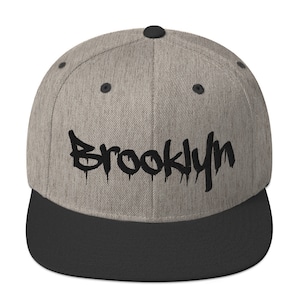 May include: A gray and black baseball cap with the word "Brooklyn" written in black dripping paint style lettering.