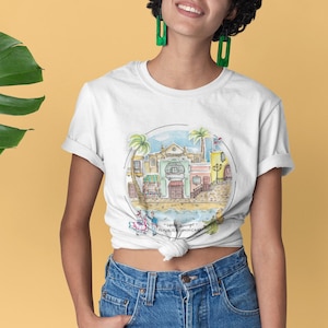 May include: White t-shirt with a colorful illustration of a cityscape with palm trees and the text "Santo Domingo, Republica Dominicana".