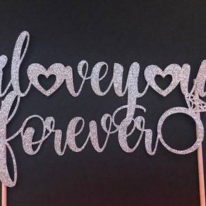 May include: Silver glitter cake topper with the text "I love you forever" and a ring with a diamond.