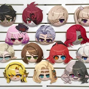 Puede incluir: Una colección de catorce parches circulares con cabezas de personajes estilo anime dispuestos sobre un tablero blanco con listones. Cada parche presenta un personaje único con colores de cabello, ojos y expresiones faciales distintos.