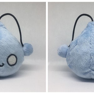 May include: A light blue plush toy shaped like a teardrop with a black string attached. The toy has a cute face with black eyes and a small mouth.