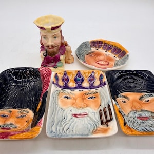 以下が含まれることがあります： ヴィンテージの陶器製の置物と食器のコレクション。ひげを生やした男性の小さな花瓶と、王冠と帽子をかぶった男性の顔が描かれたお皿がいくつかあります。カラーパレットには、ベージュ、紫、オレンジ、黒の色合いが含まれています。