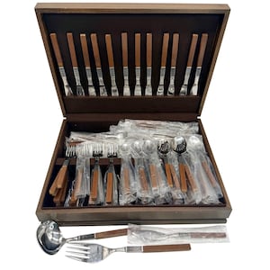 Op de afbeelding: Een houten bestekset met roestvrijstalen gebruiksvoorwerpen en bruine houten handvatten. De set bevat vorken, messen, lepels en serveerstukken, allemaal netjes gerangschikt in een donkere houten kist met een bruin interieur. De set is ideaal voor formeel dineren.