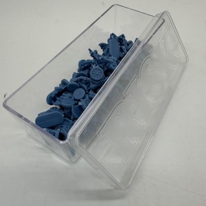 May include: A clear plastic box, partially open, containing small blue game pieces. The lid is embossed with the word "RISK". The box is filled with miniature figures and other game components, likely for a board game.