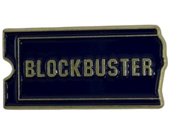 May include: A rectangular pin with a dark blue background and the word "BLOCKBUSTER" in gold lettering. The pin has a gold border and a ticket-like shape with a notch on the left side.