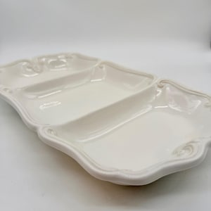 Può includere: Un piatto da portata bianco diviso in tre sezioni, con un bordo smerlato decorativo. Ideale per servire antipasti o snack. Il piatto ha una finitura lucida e un design classico.