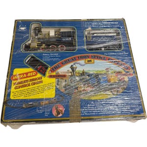 May include: A boxed toy train set, with a black and gold locomotive and carriages. The packaging features the text "The Great Iron Spike Express Railroad" and "Infra-Red Wireless Remote Control Center". The box is wrapped in clear plastic.